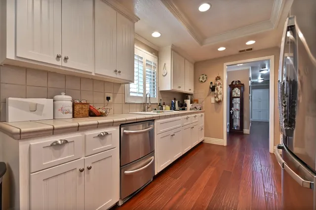 a kitchen with granite countertop a refrigerator a sink dishwasher and white cabinets with wooden floor