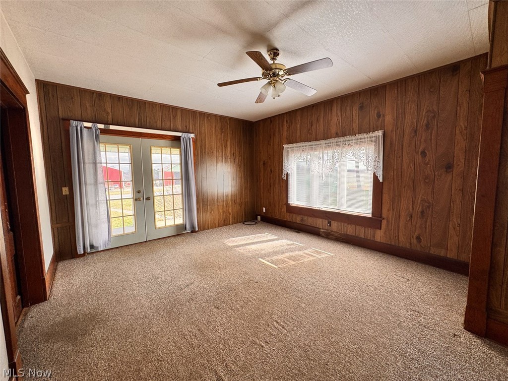 15 Glecoe Road Southwest Carrollton, OH 44615 - Photo 43 of 50 Empty room with french doors, ceiling fan, light carpet, wooden walls, and a textured ceiling