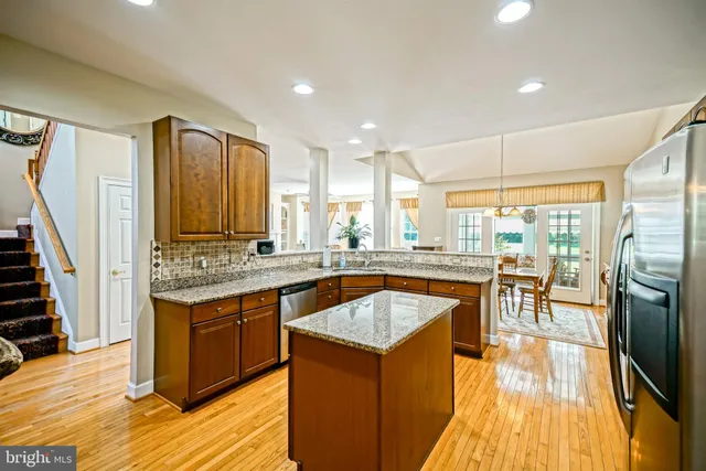 a kitchen with stainless steel appliances granite countertop a stove top oven a sink dishwasher a dining table and chairs with wooden floor