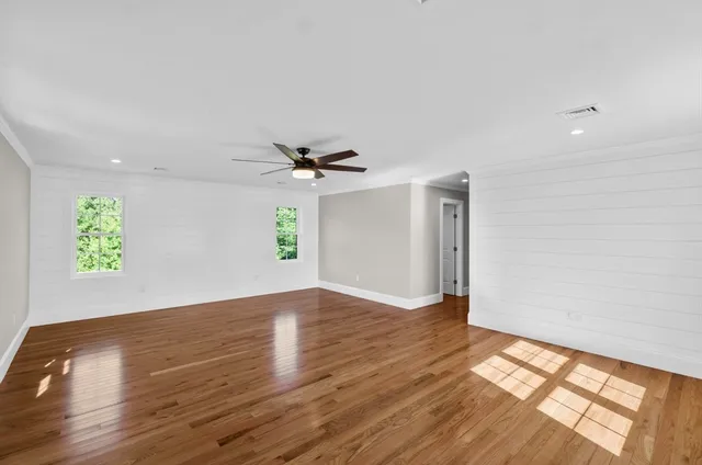 an empty room with wooden floor chandelier fan and windows
