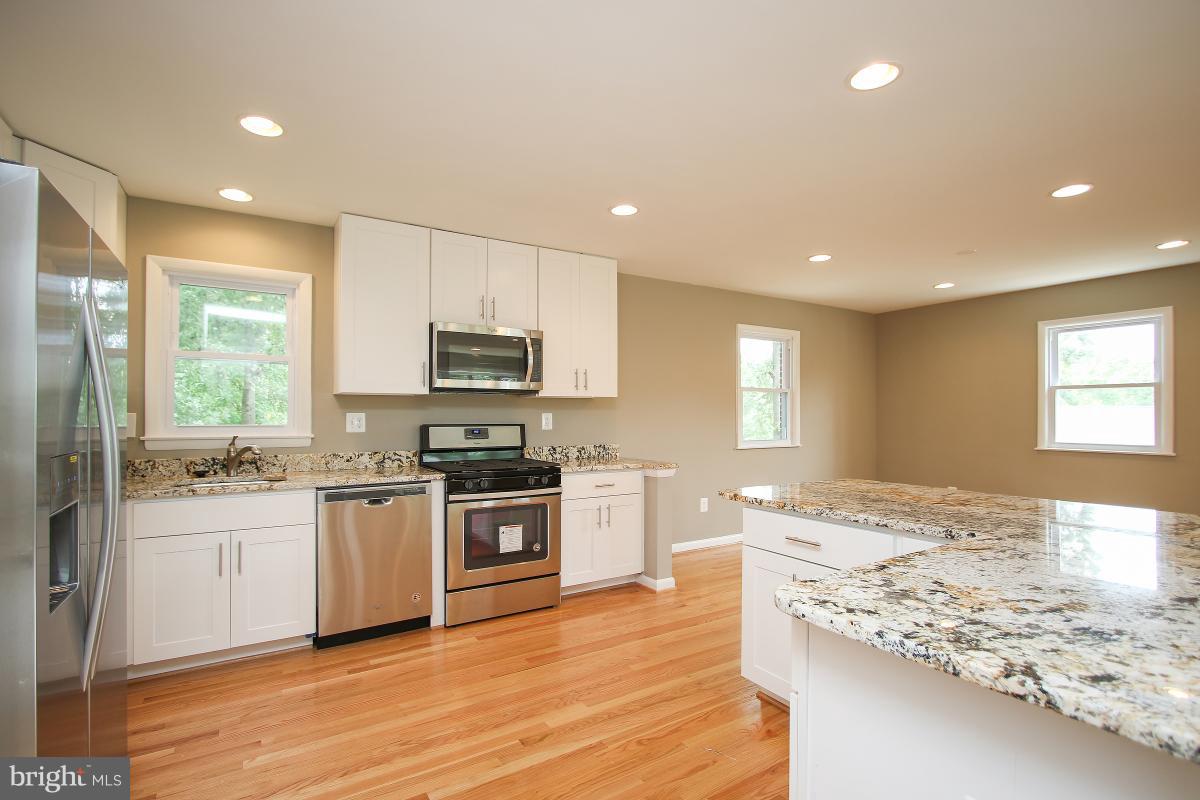 6903 Presley Road Lanham, MD 20706 - Photo 10 of 28 a large kitchen with kitchen island granite countertop a stove top oven a sink a dining table and chairs
