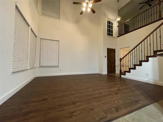 a view of an empty room with wooden floor and fan