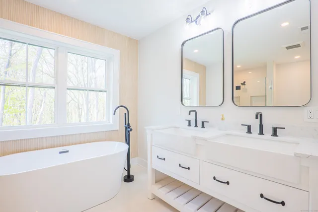 a bathroom with a tub double sink window and mirror