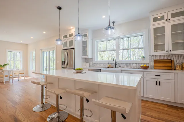 a large kitchen with granite countertop a large island in the center a sink stainless steel appliances and a large window