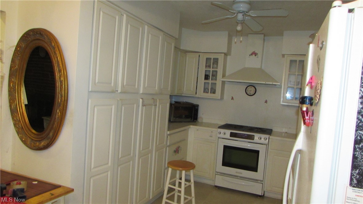 18375 Alexander Road Walton Hills, OH 44146 - Photo 12 of 25 Kitchen featuring white cabinets, wall chimney range hood, white appliances, and ceiling fan