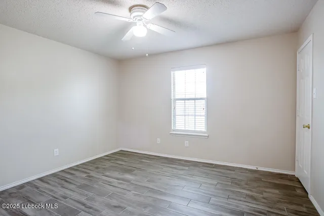 an empty room with wooden floor fan and windows