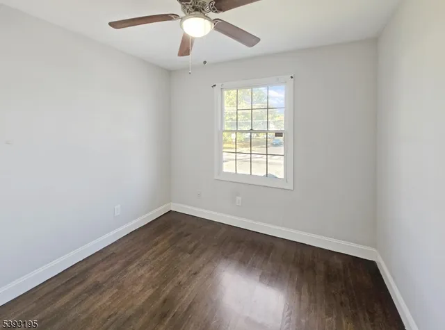 an empty room with wooden floor fan and windows