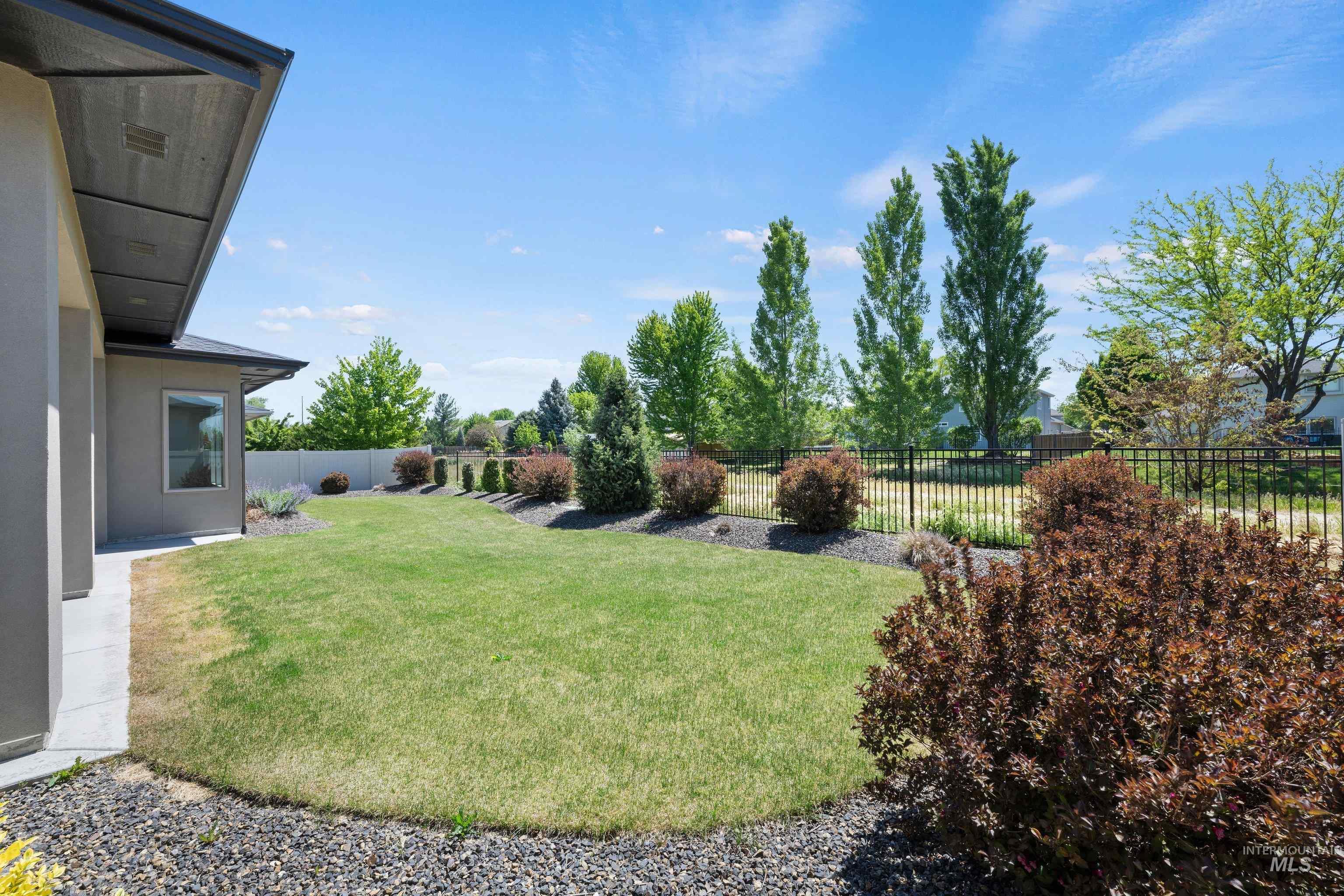 4447 East Copper Point Drive Meridian, ID 83642 - Photo 37 of 41 Expansive backyard featuring a lush lawn, mature trees, and a black wrought iron fence