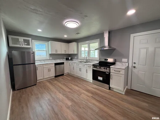 a kitchen with stainless steel appliances granite countertop a refrigerator a sink dishwasher a stove and white cabinets with wooden floor