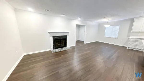 an empty room with wooden floor fireplace and windows