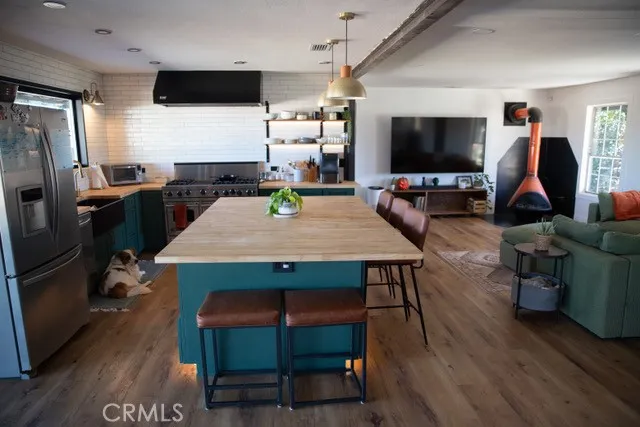 a kitchen with stainless steel appliances kitchen island granite countertop a stove a refrigerator a sink a dining table and chairs with wooden floor