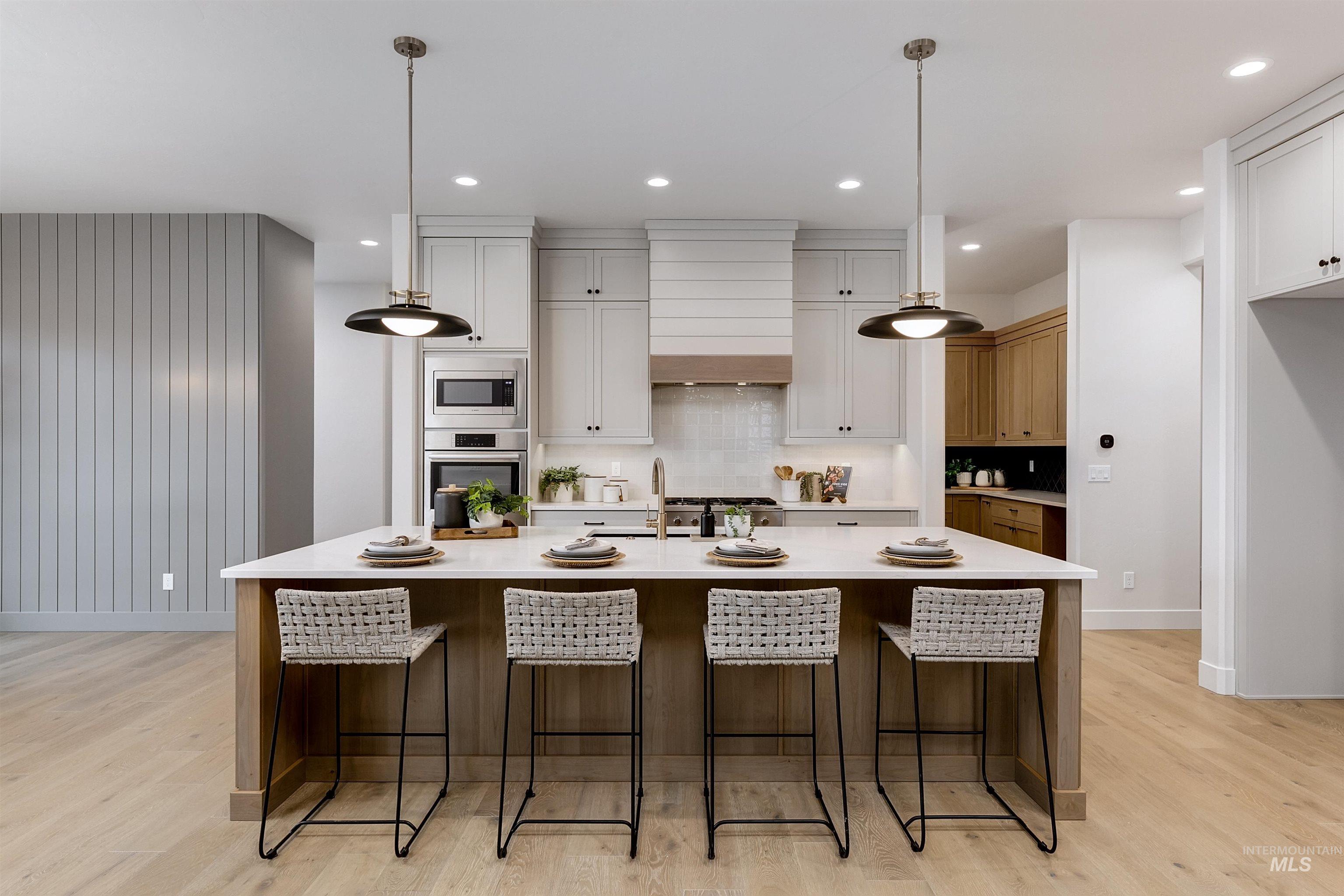 13331 North Spring Creek Way Boise, ID 83714 - Photo 6 of 43 Two tone kitchen with a breakfast bar, dual tone cabinetry, pendant lighting, a center island with sink, and light wood-type flooring
