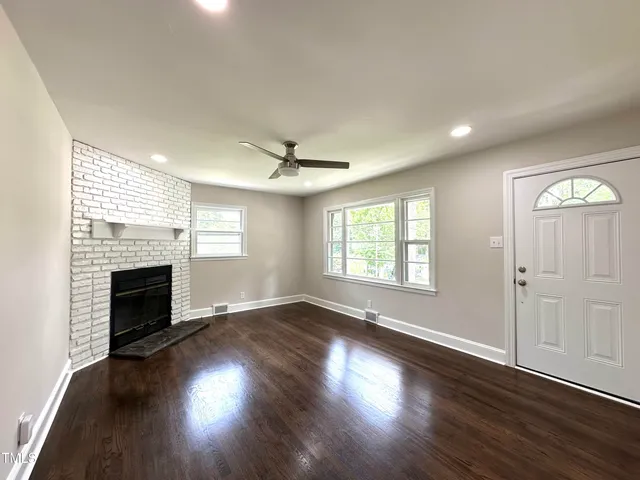 an empty room with wooden floor fireplace and windows