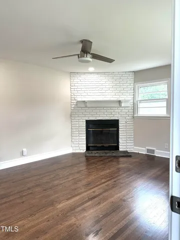 a view of an empty room with wooden floor fireplace and a window