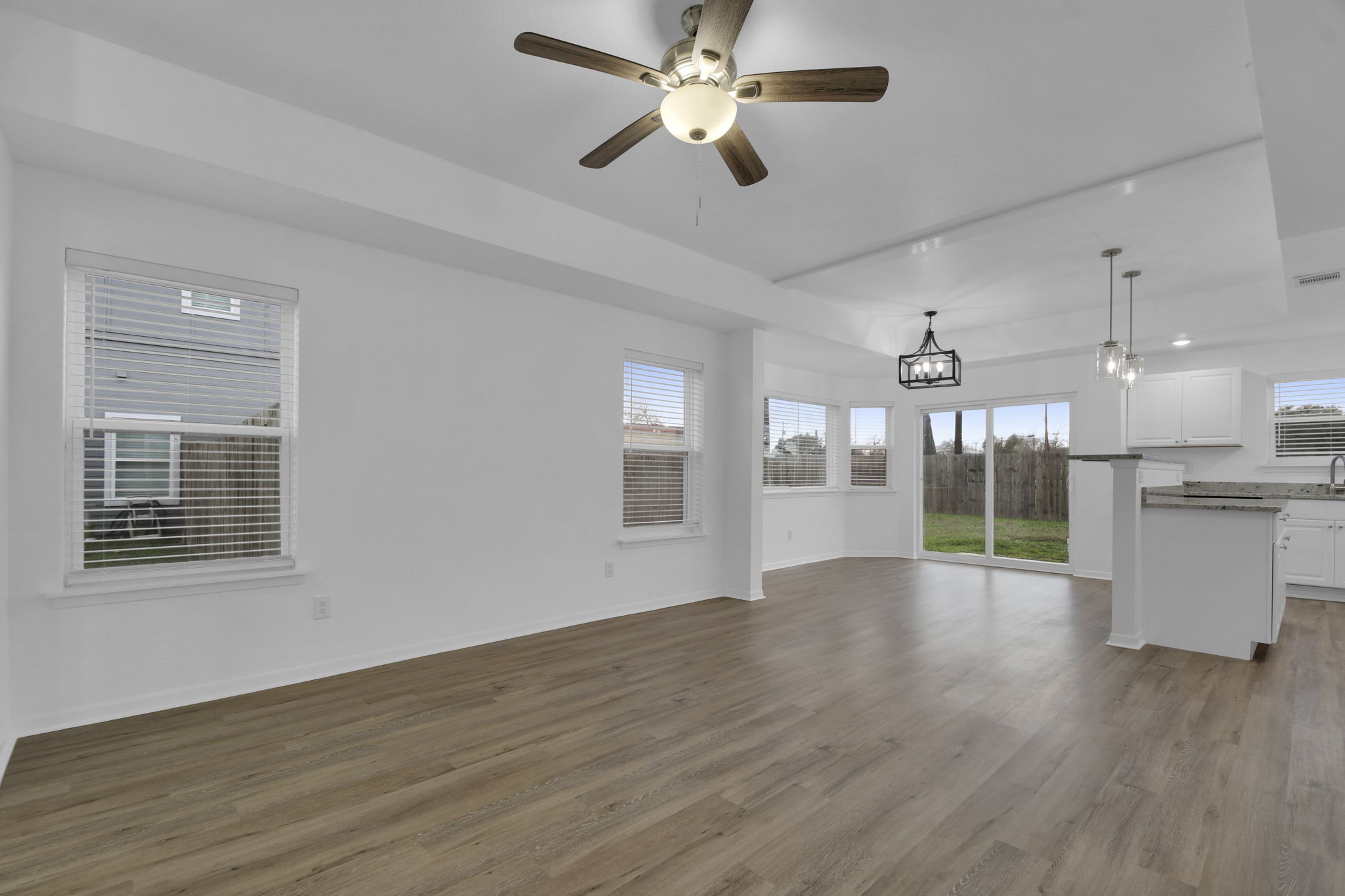 1008 East Fannin Street Luling, TX 78648 - Photo 6 of 13 Unfurnished living room with ceiling fan, dark wood-style floors, a tray ceiling, and a chandelier
