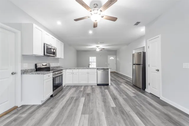 a large kitchen with kitchen island a stove a sink dishwasher a refrigerator and white cabinets with wooden floor