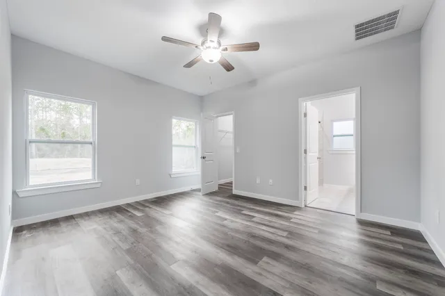 an empty room with wooden floor ceiling fan and windows