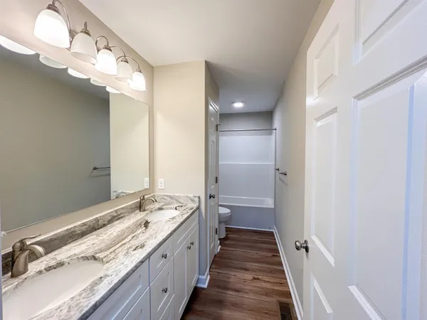 a view of a hallway with wooden floor and a bathroom