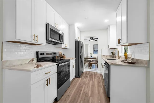 a kitchen with stainless steel appliances a sink dishwasher a stove top oven a refrigerator with grey cabinets and wooden floor