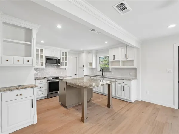 a kitchen with stainless steel appliances a stove a sink dishwasher a refrigerator white cabinets and wooden floor