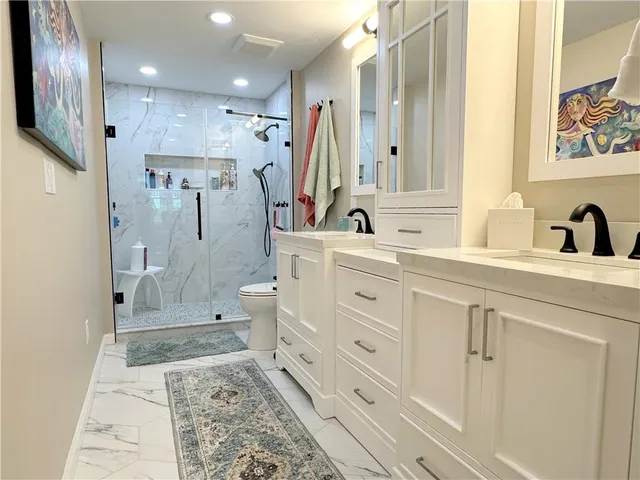 a bathroom with a double vanity sink a toilet a mirror and shower