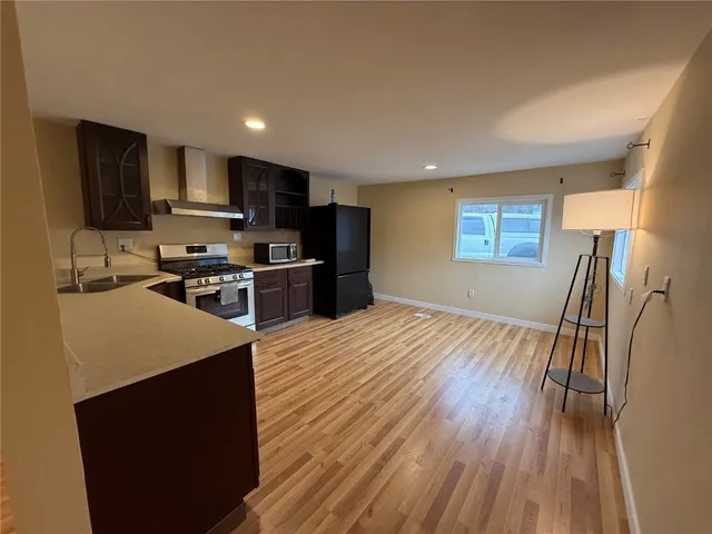 a large kitchen with stainless steel appliances a large counter top a stove a refrigerator a sink dishwasher and a fireplace with wooden floor