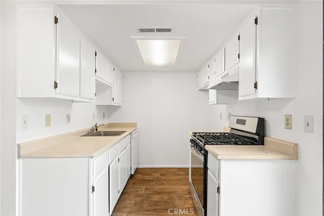a kitchen with stainless steel appliances a white stove top oven a sink a refrigerator and white cabinets