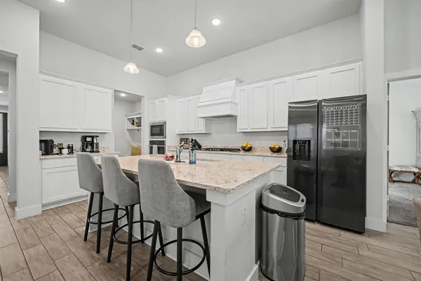 a kitchen with stainless steel appliances granite countertop a refrigerator a sink a stove and white cabinets with wooden floor