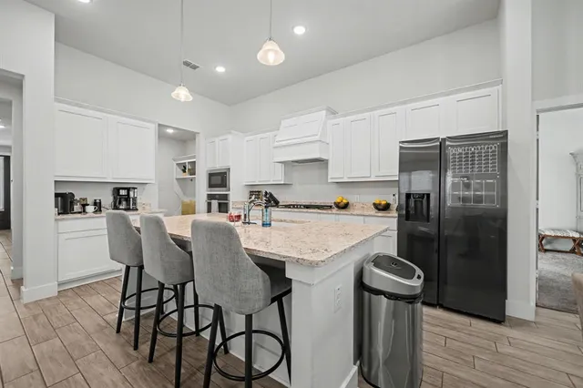 a kitchen with stainless steel appliances granite countertop a refrigerator a sink a stove and white cabinets with wooden floor