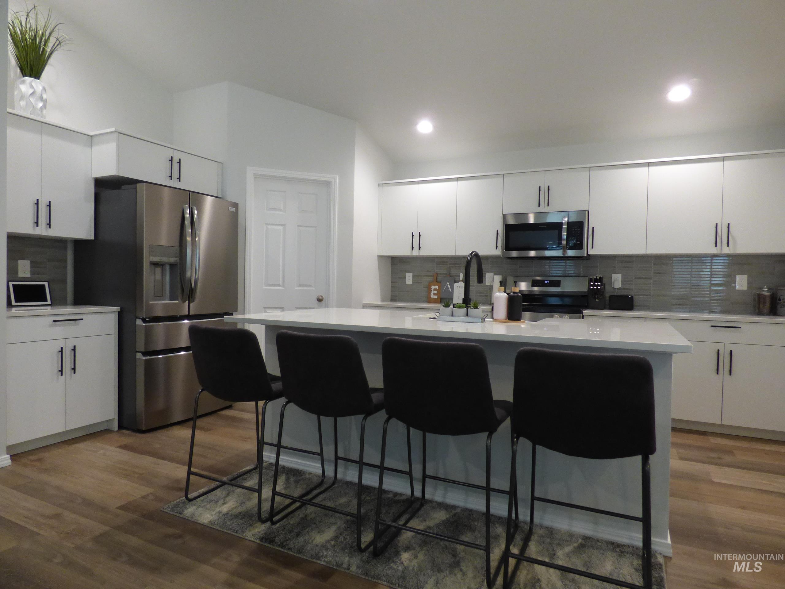 2708 East Buckaroo Drive Kuna, ID 83634 - Photo 7 of 48 Contemporary kitchen featuring a large central island with seating, extensive white cabinetry, stainless steel appliances, and wood-finish flooring