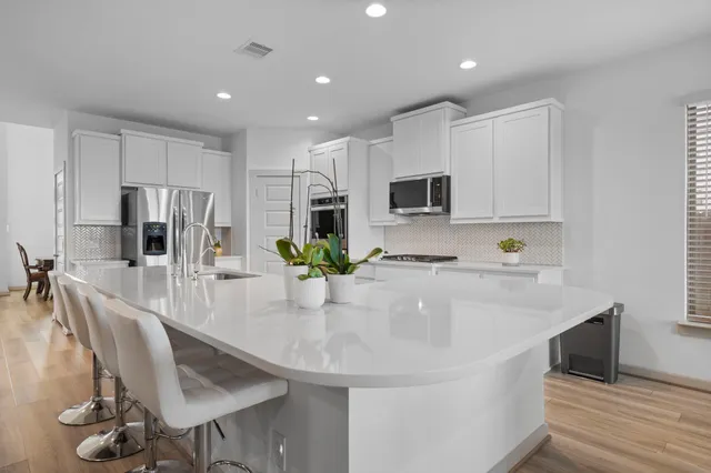 a kitchen with kitchen island granite countertop a sink a stove a refrigerator cabinets and chairs