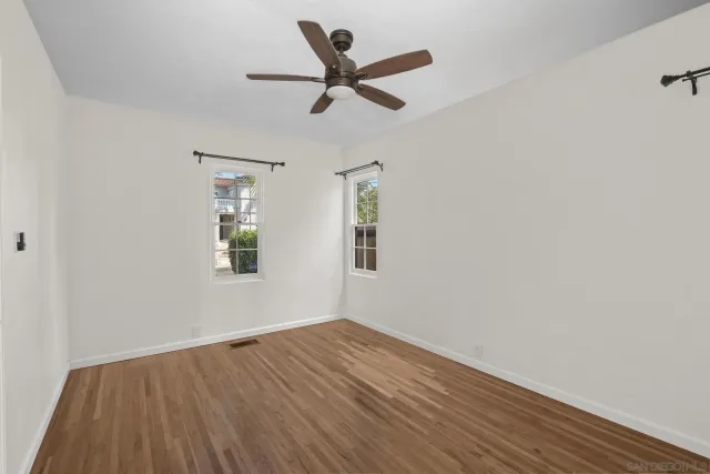 an empty room with wooden floor ceiling fan and window