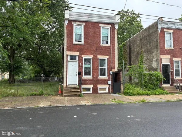 a view of a brick house with a yard plants and large trees
