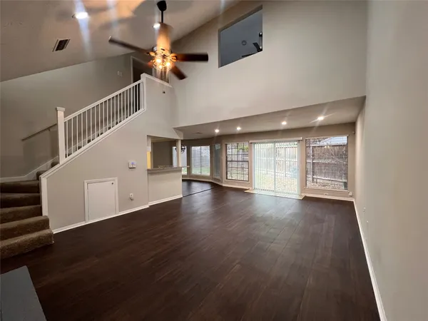a view of an empty room with wooden floor and a ceiling fan