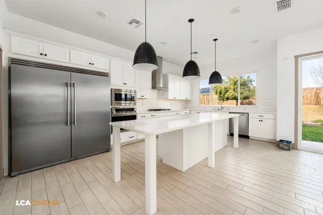 a kitchen with stainless steel appliances a refrigerator a sink a stove and white cabinets with wooden floor