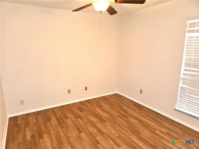 a view of empty room with wooden floor and fan