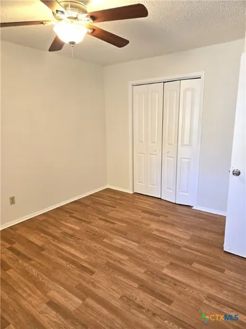 a view of an empty room with wooden floor and a ceiling fan