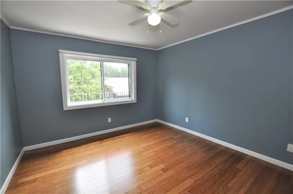 a view of an empty room with wooden floor and a ceiling fan