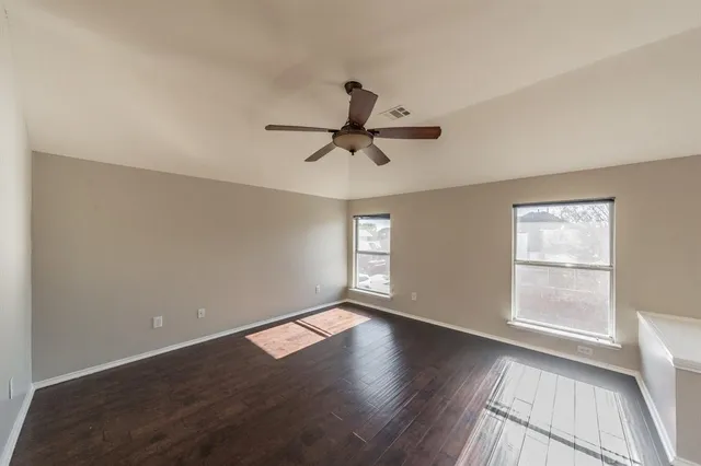 an empty room with wooden floor fan and windows