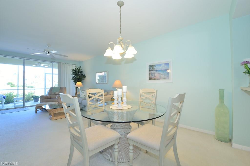 4960 Deerfield Way, Unit E102 Naples, FL 34110 - Photo 6 of 19 a dining room with furniture a large window and a chandelier
