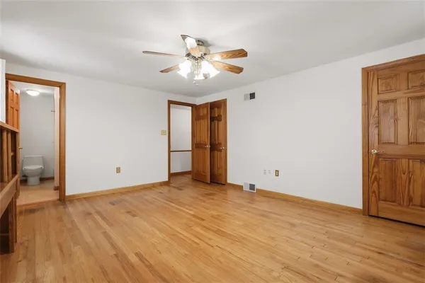 a view of an empty room with wooden floor and a ceiling fan