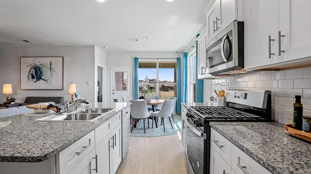 a kitchen with granite countertop stainless steel appliances a sink a stove a table and chairs