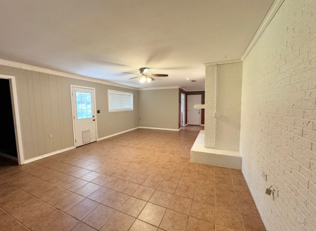 1225 Lake Terrace Drive Elgin, TX 78621 - Photo 6 of 28 Empty room with ornamental molding, brick wall, light tile patterned floors, a multi sided fireplace, and ceiling fan