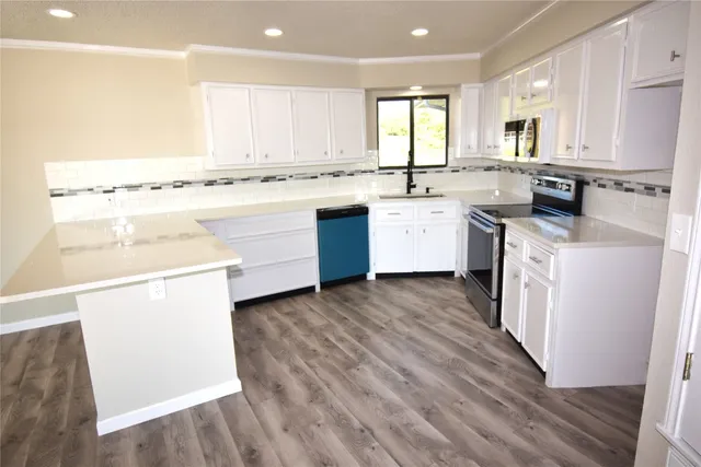 a kitchen with a white stove top oven sink and white cabinets with wooden floor