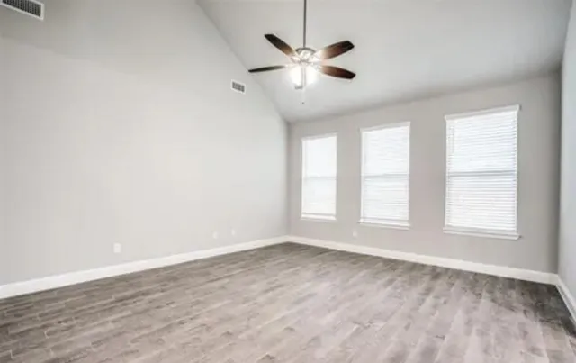 an empty room with wooden floor fan and windows