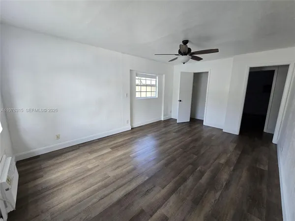 an empty room with wooden floor ceiling fan and window