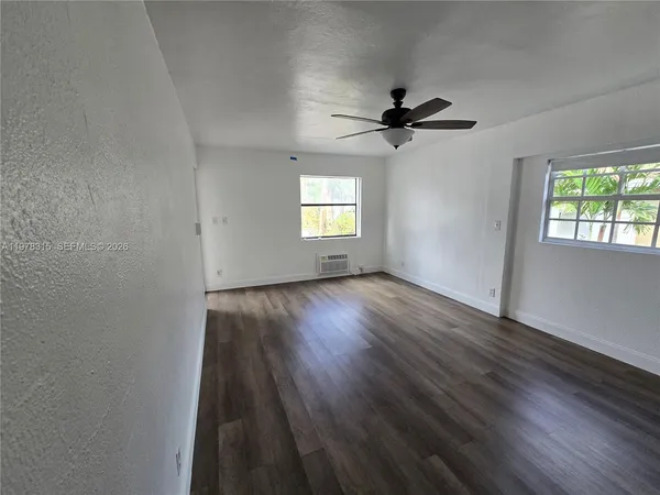 an empty room with wooden floor ceiling fan and windows
