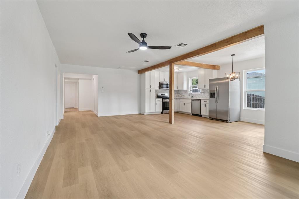Unfurnished living room with ceiling fan, light wood finished floors, beamed ceiling, and a chandelier