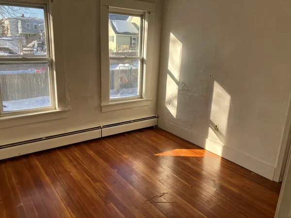 a view of an empty room with wooden floor and a window