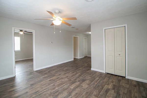 a view of an empty room with wooden floor and a ceiling fan